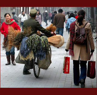 street scene in China showing man pushing bicycle loaded with wares walking alongside stylish shoppers