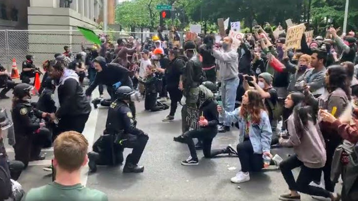 group of police kneel before protesters, some of whom offer thanks 